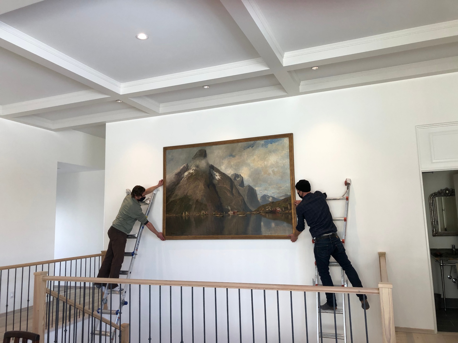 Raven Art Services team installing a framed landscape painting in a mountain home