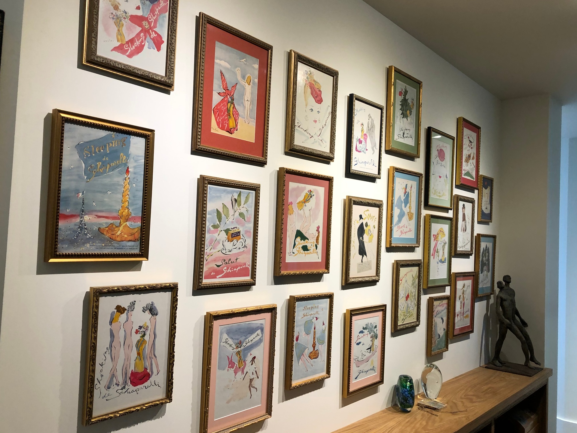 Salon-style gallery wall of framed Schiaparelli watercolor prints in gold frames